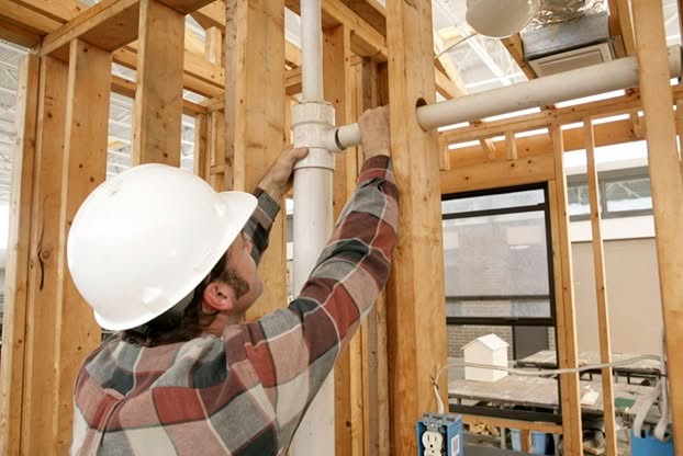 A construction worker wearing a hard hat and helmet while working on a wall at a construction site.